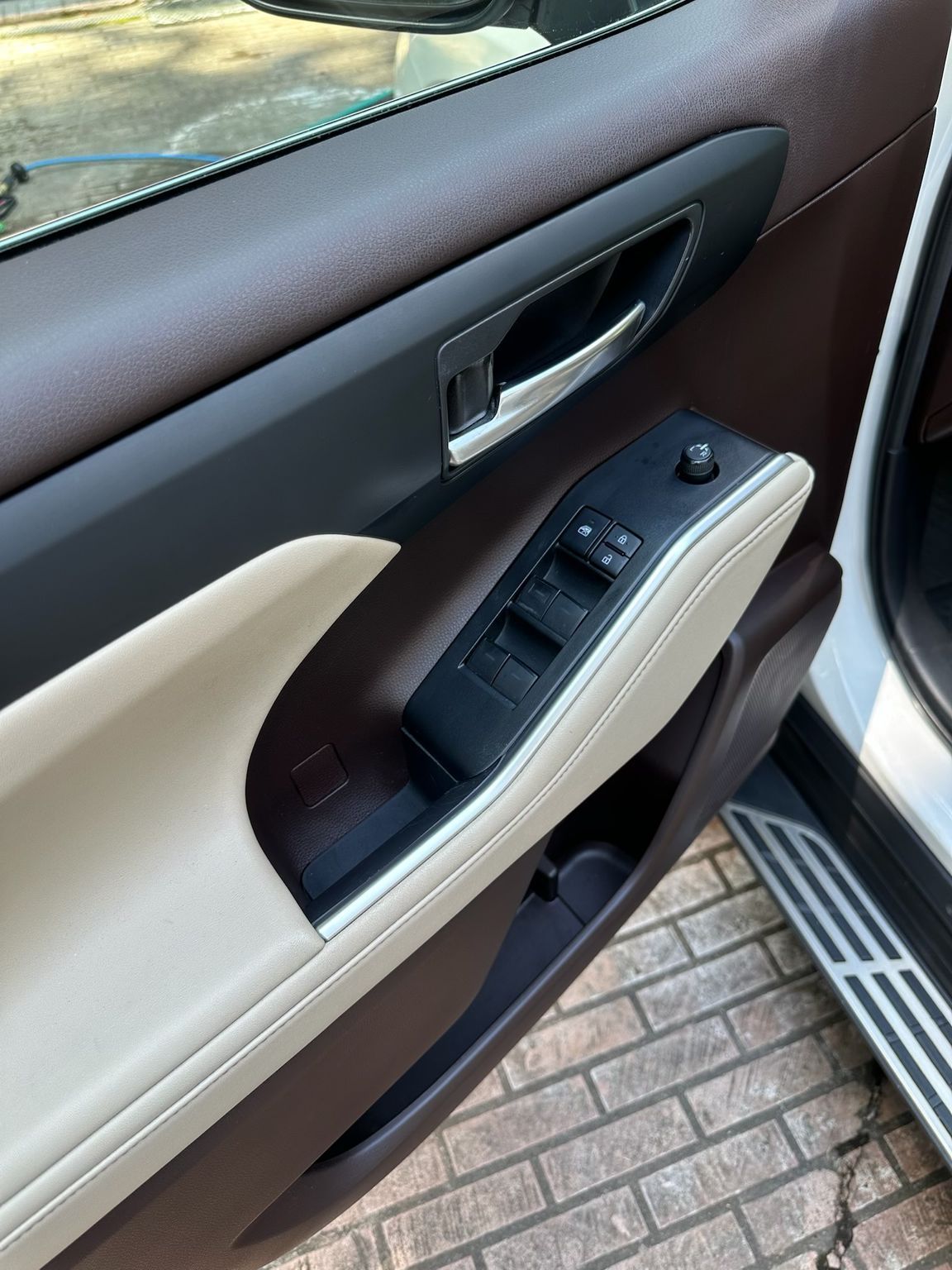A car interior door panel featuring a cream leather armrest, brown trim, and a black power window control switch console.