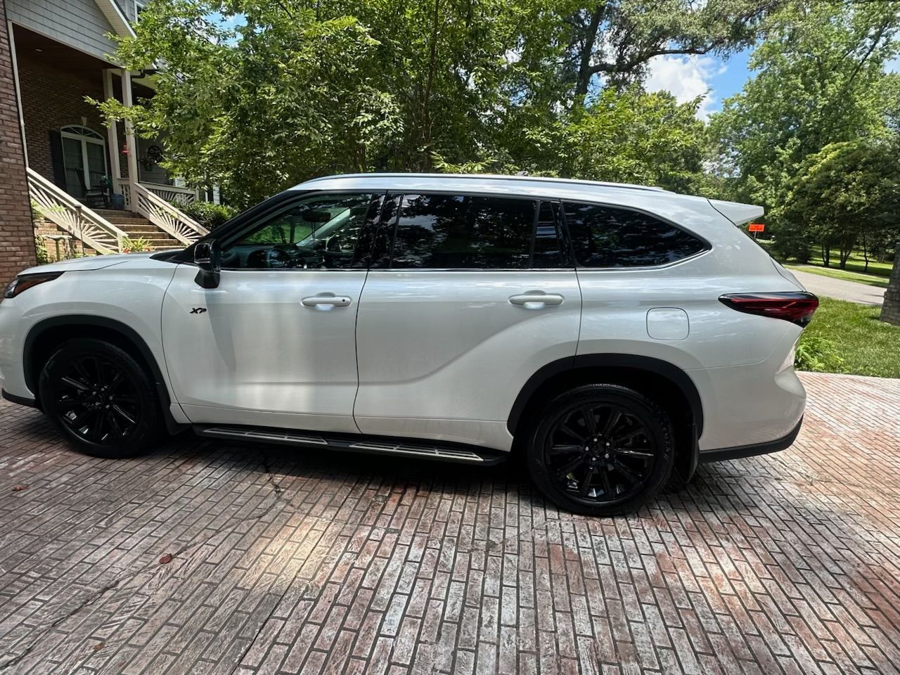 A white SUV parked on a brick driveway in front of a house surrounded by trees.