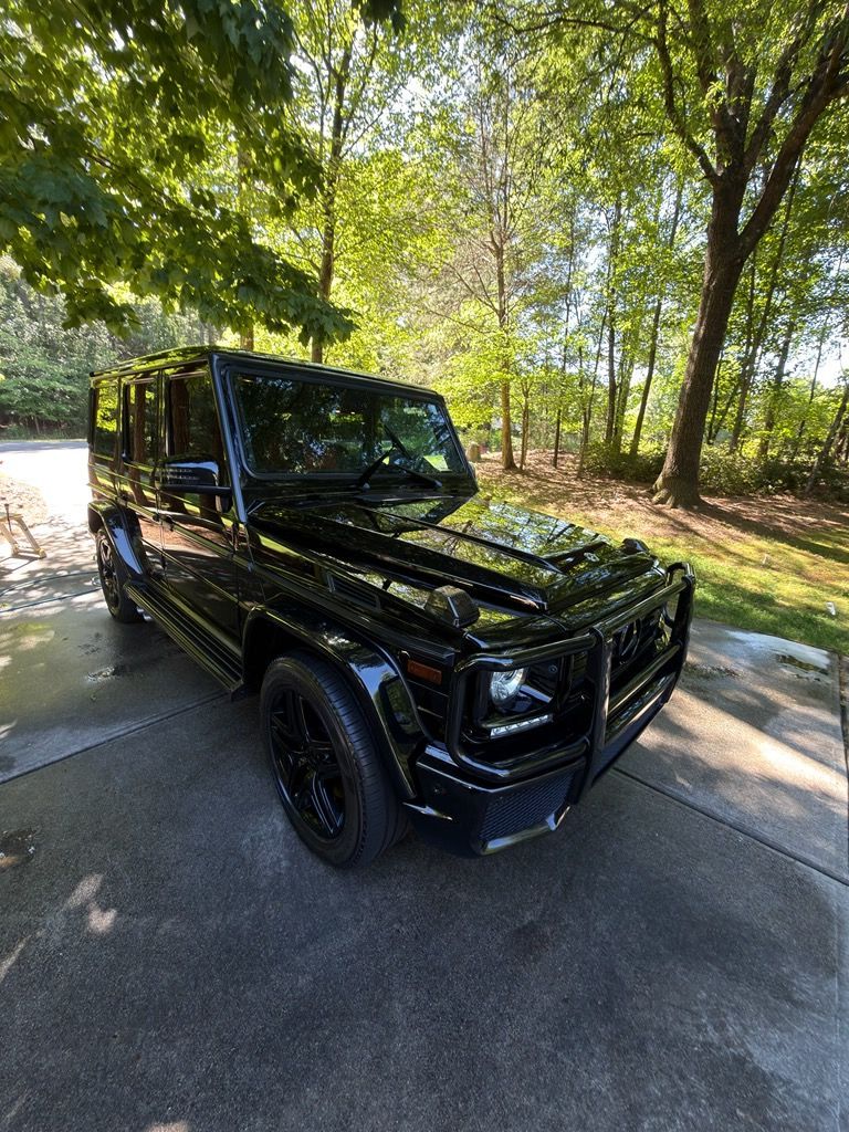 Black Mercedes G-Class SUV parked on a wooded roadside in sunlight