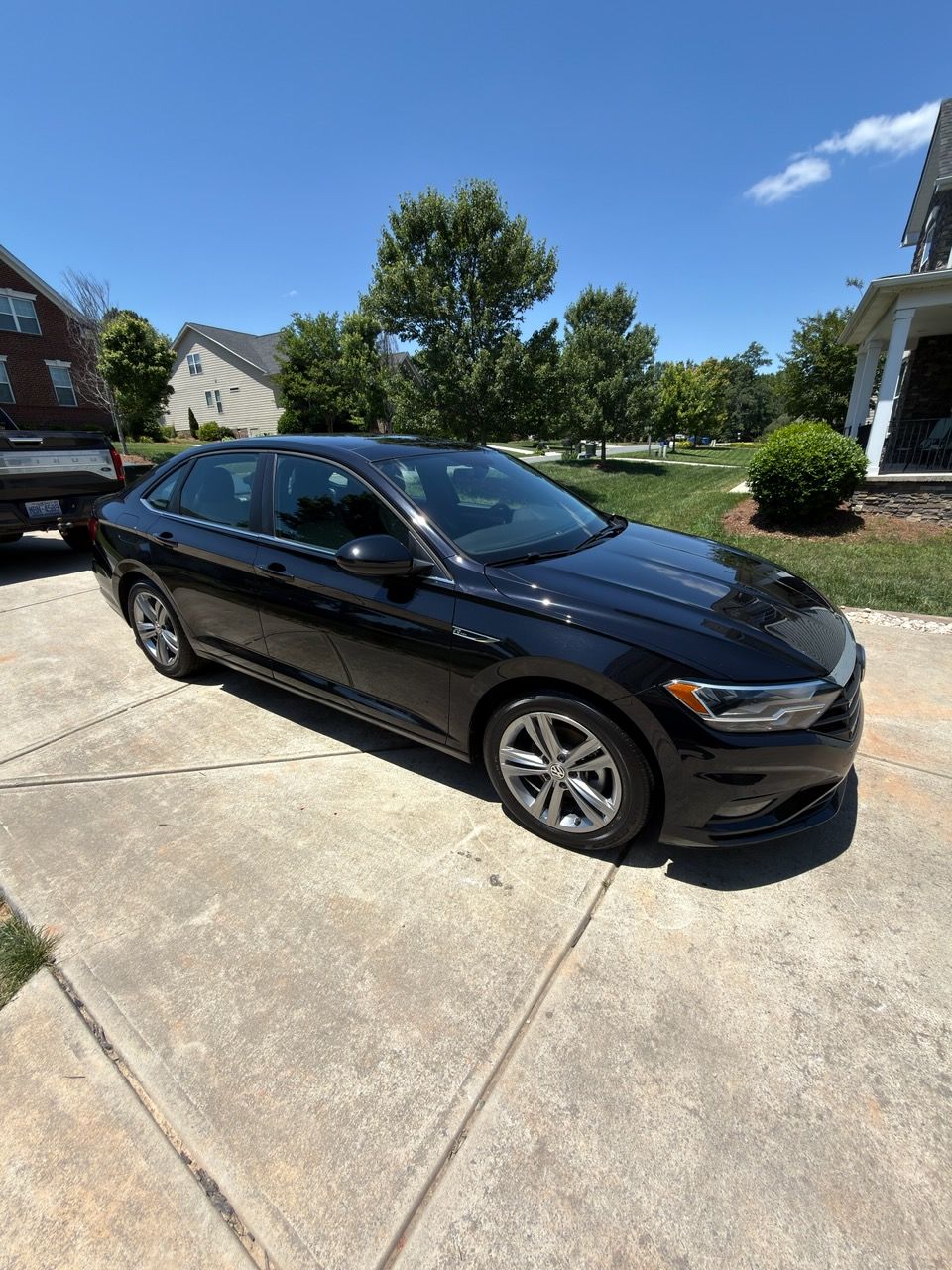 Black sedan parked in a sunny suburban driveway beside a lawn and houses