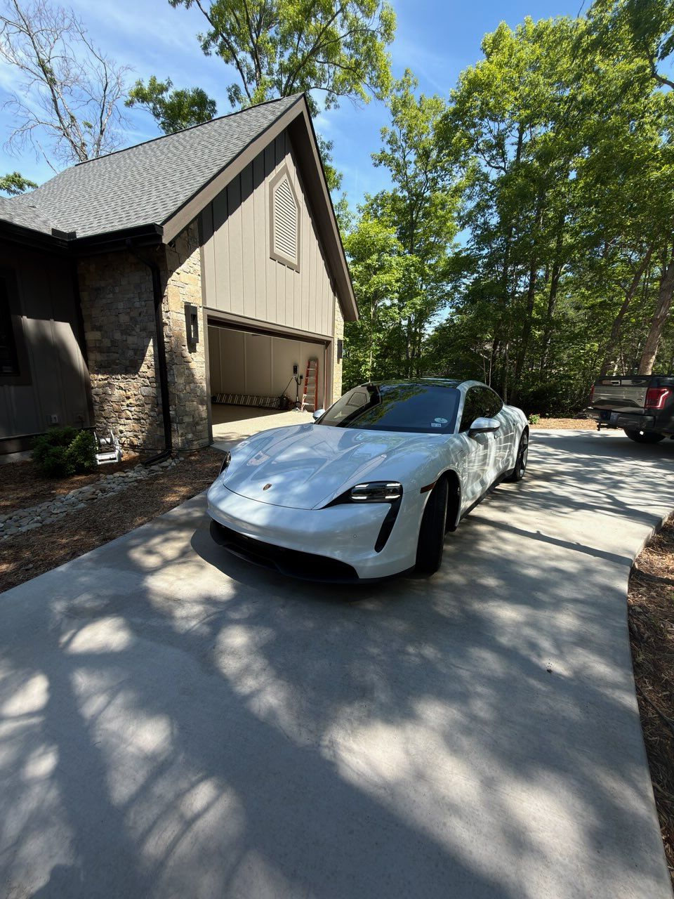 White sports car parked in a sunlit driveway beside a house and trees