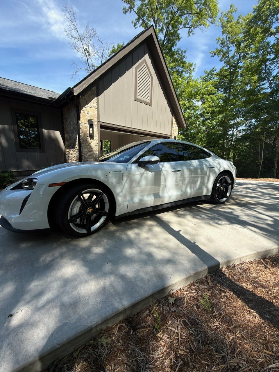 Silver sedan parked in a driveway beside a house with trees and shadows overhead
