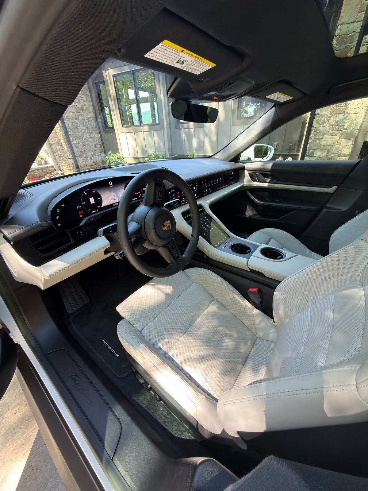 Driver’s seat view of a modern car interior with white leather seats and black dashboard, parked outdoors