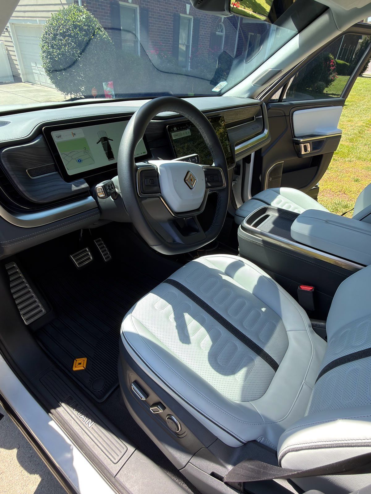 Car interior with a steering wheel, digital dashboard, and light gray front seats in sunlight