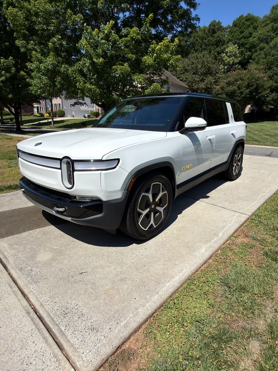 White Rivian SUV parked in a driveway beside a grassy lawn on a sunny day