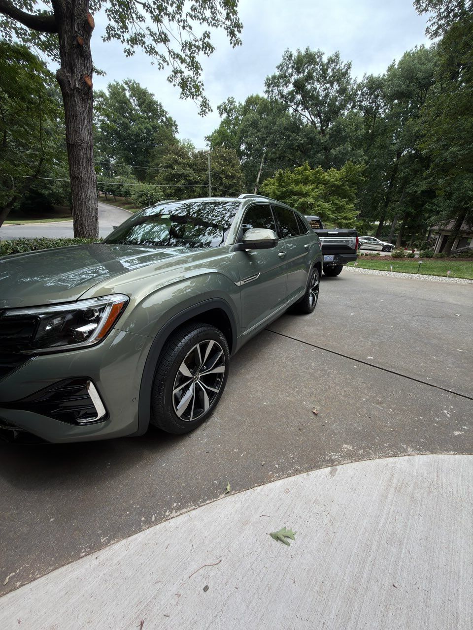 Green SUV parked on a tree-lined street with another vehicle behind it