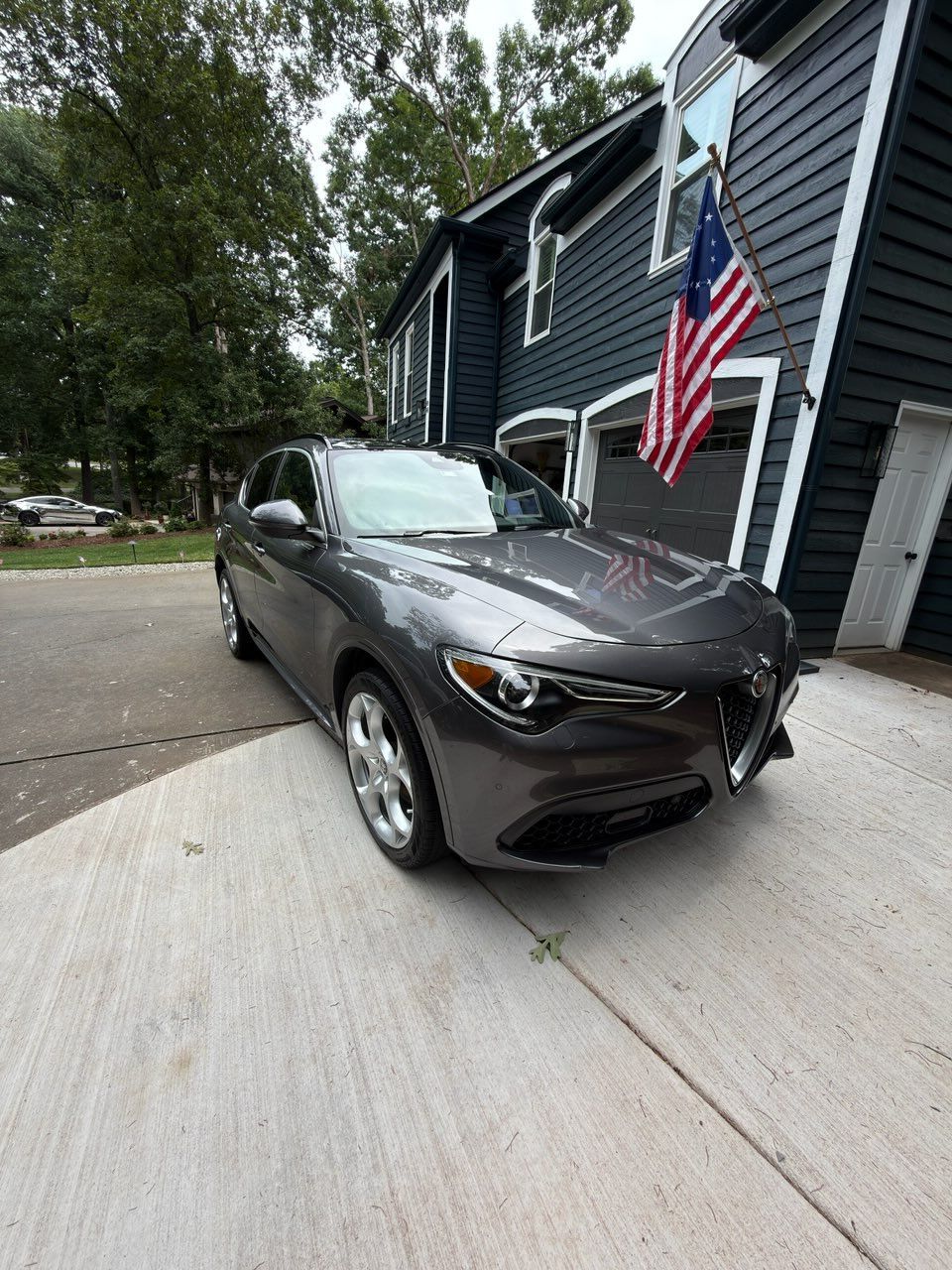 Dark gray sedan parked beside a house with an American flag on the wall