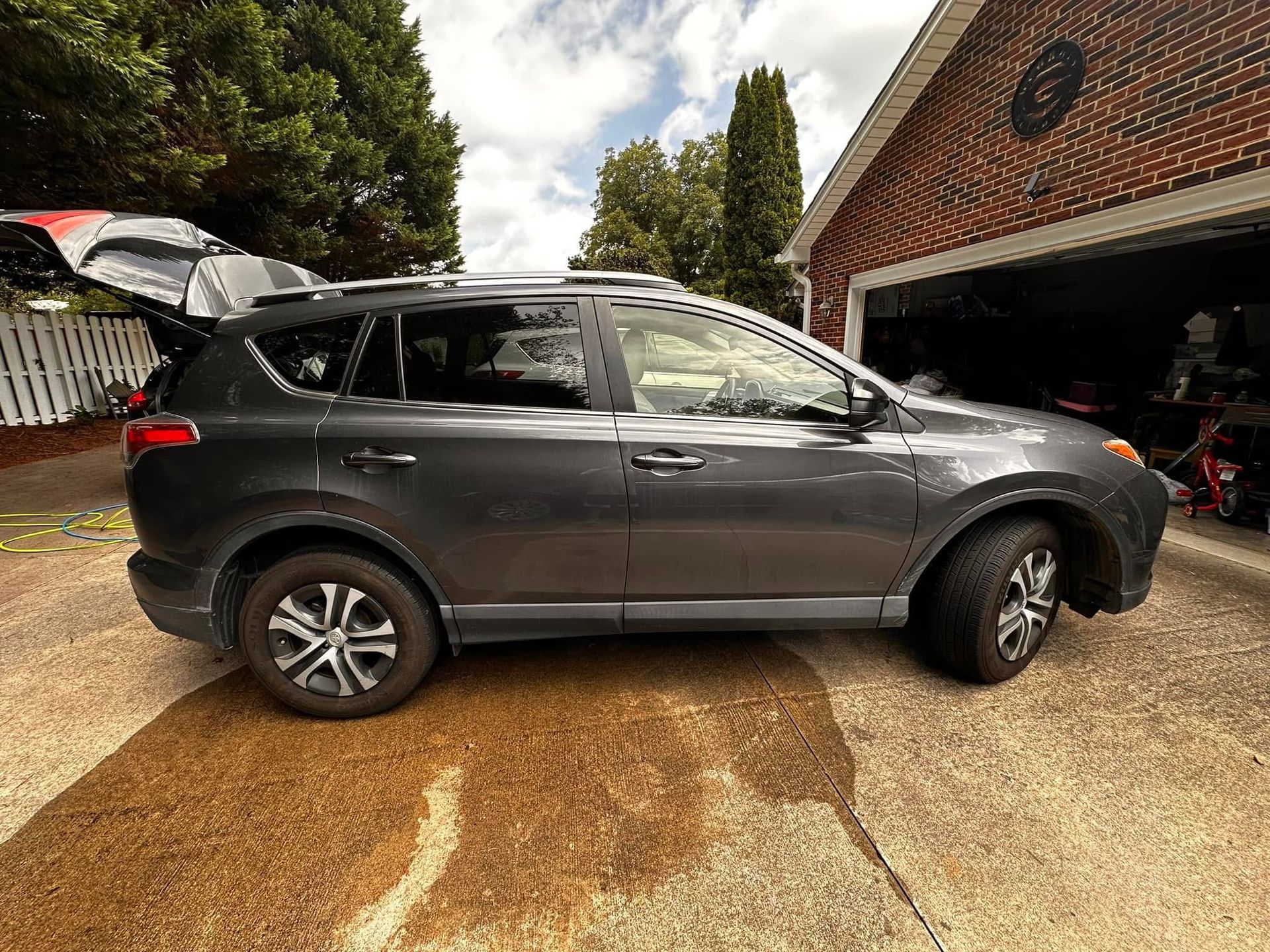 A gray SUV parked on a concrete driveway in front of a brick garage with its trunk open.