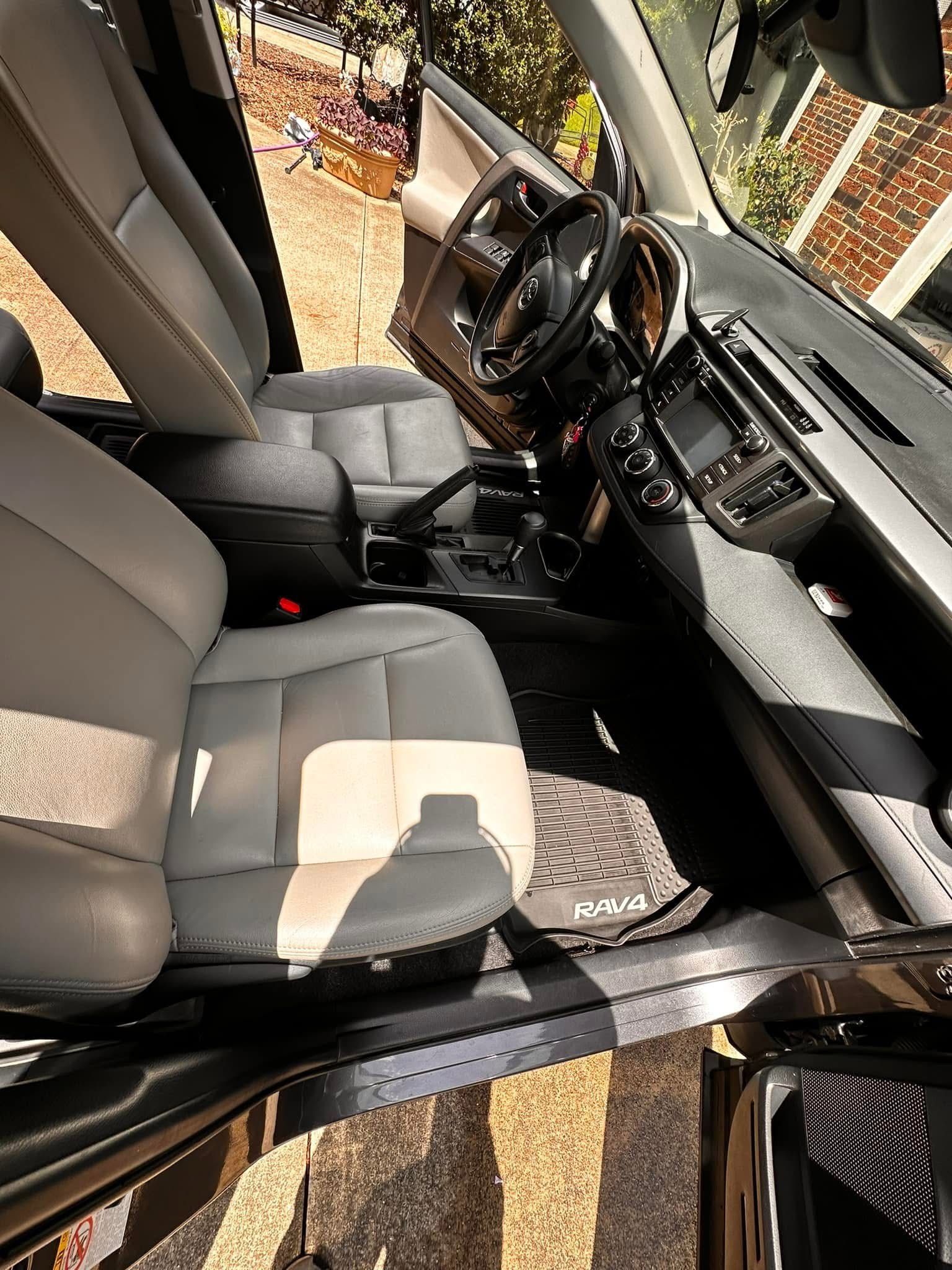 A high-angle view of a clean car interior with grey leather seats, a dark dashboard, and a textured floor mat.