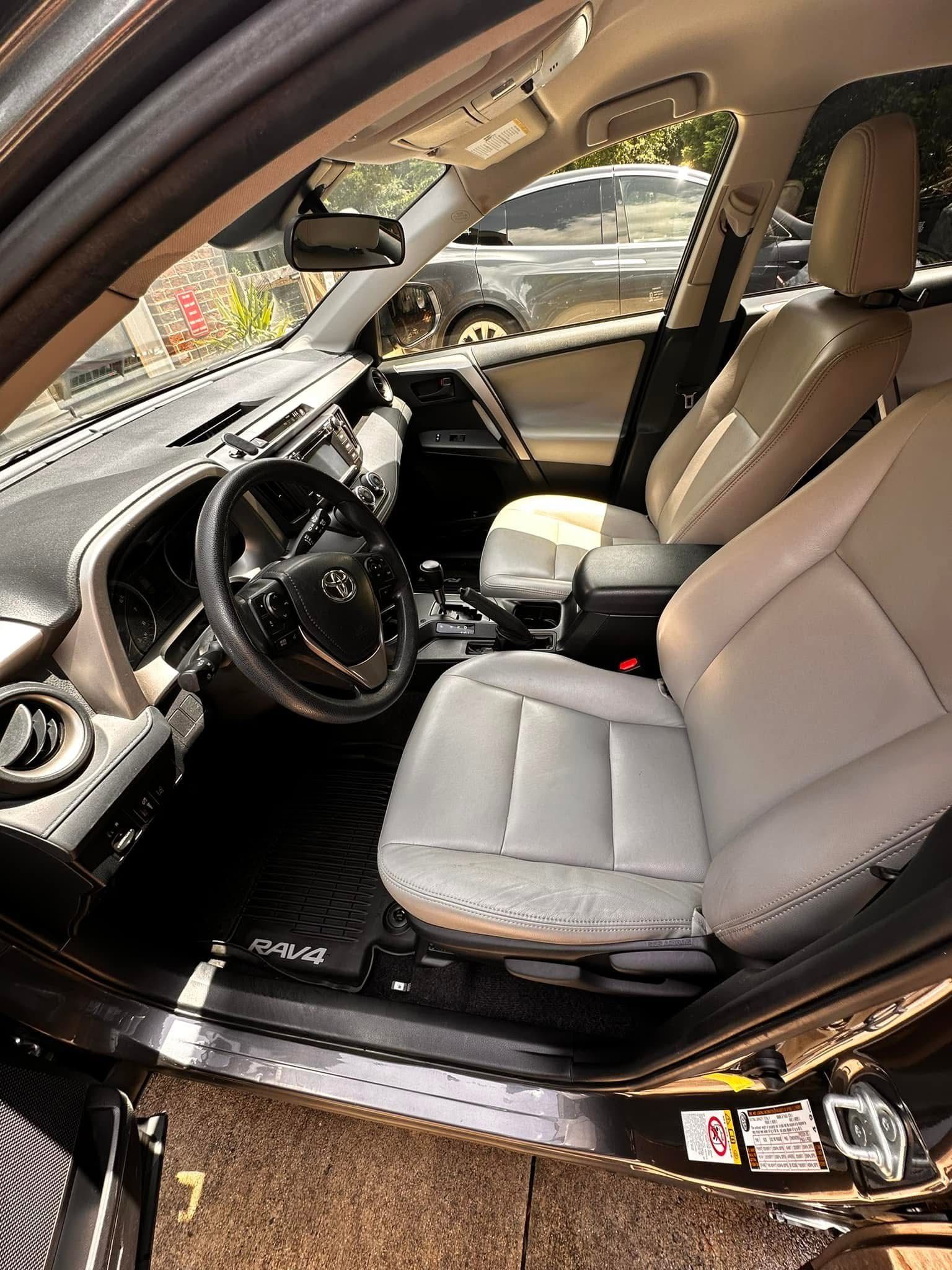 The interior of a vehicle featuring light tan leather seats, a black dashboard, and a steering wheel with Toyota branding.