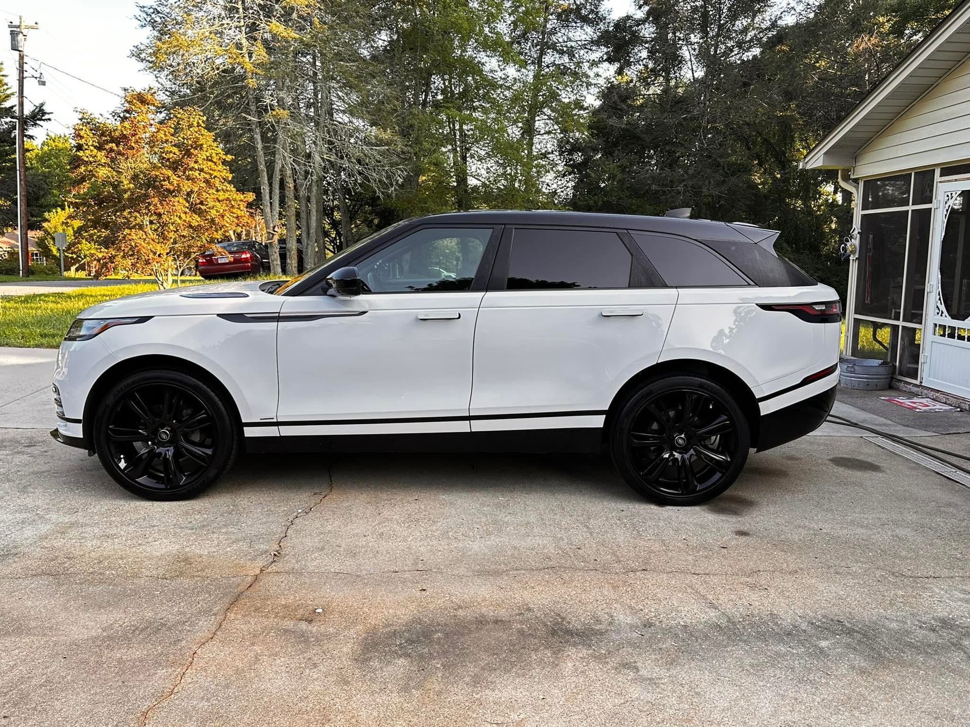A white Range Rover Velar with black trim and black wheels parked on a concrete driveway in front of a house.