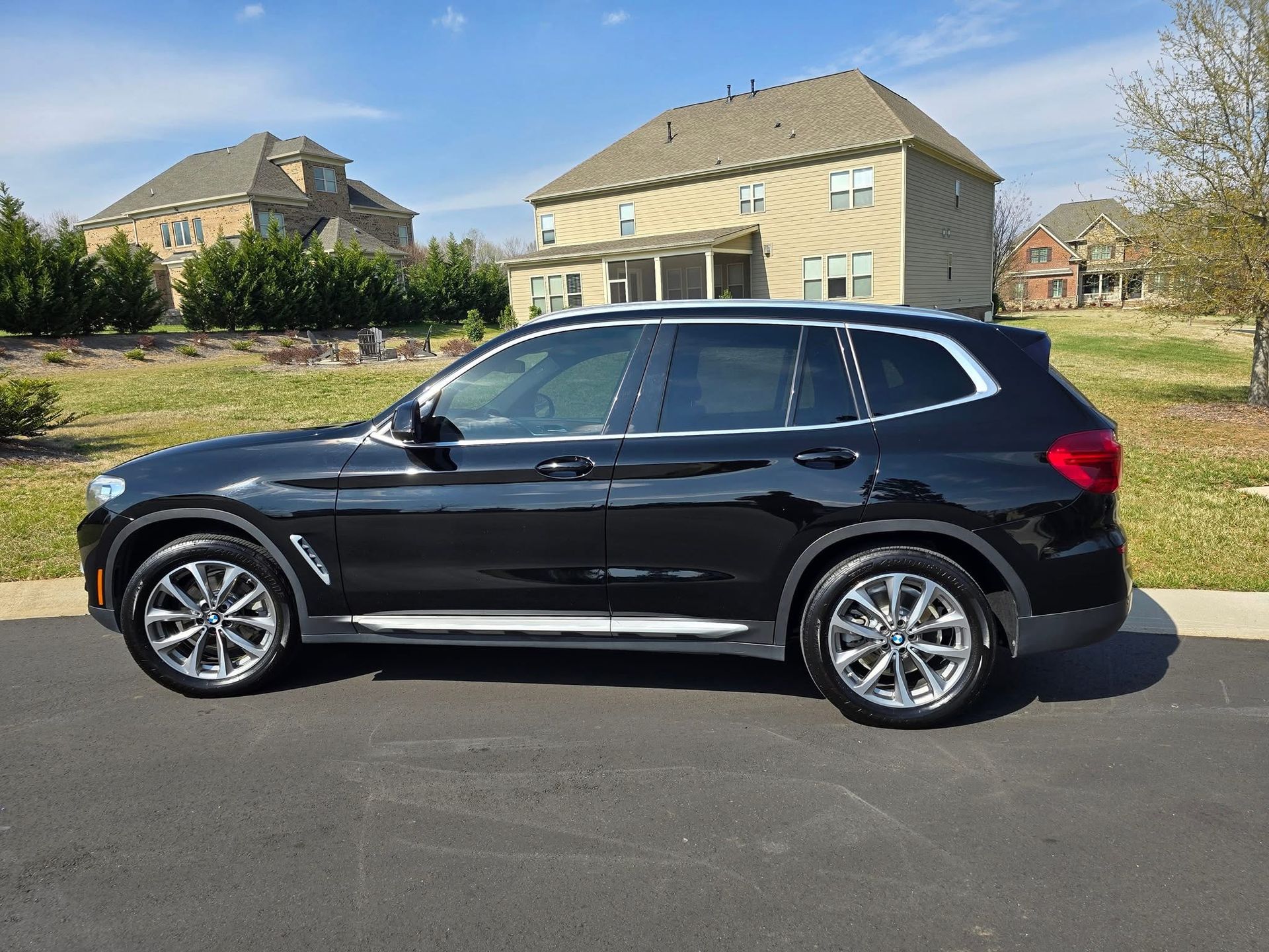 A black BMW SUV parked on an asphalt driveway in front of a suburban house on a sunny day.