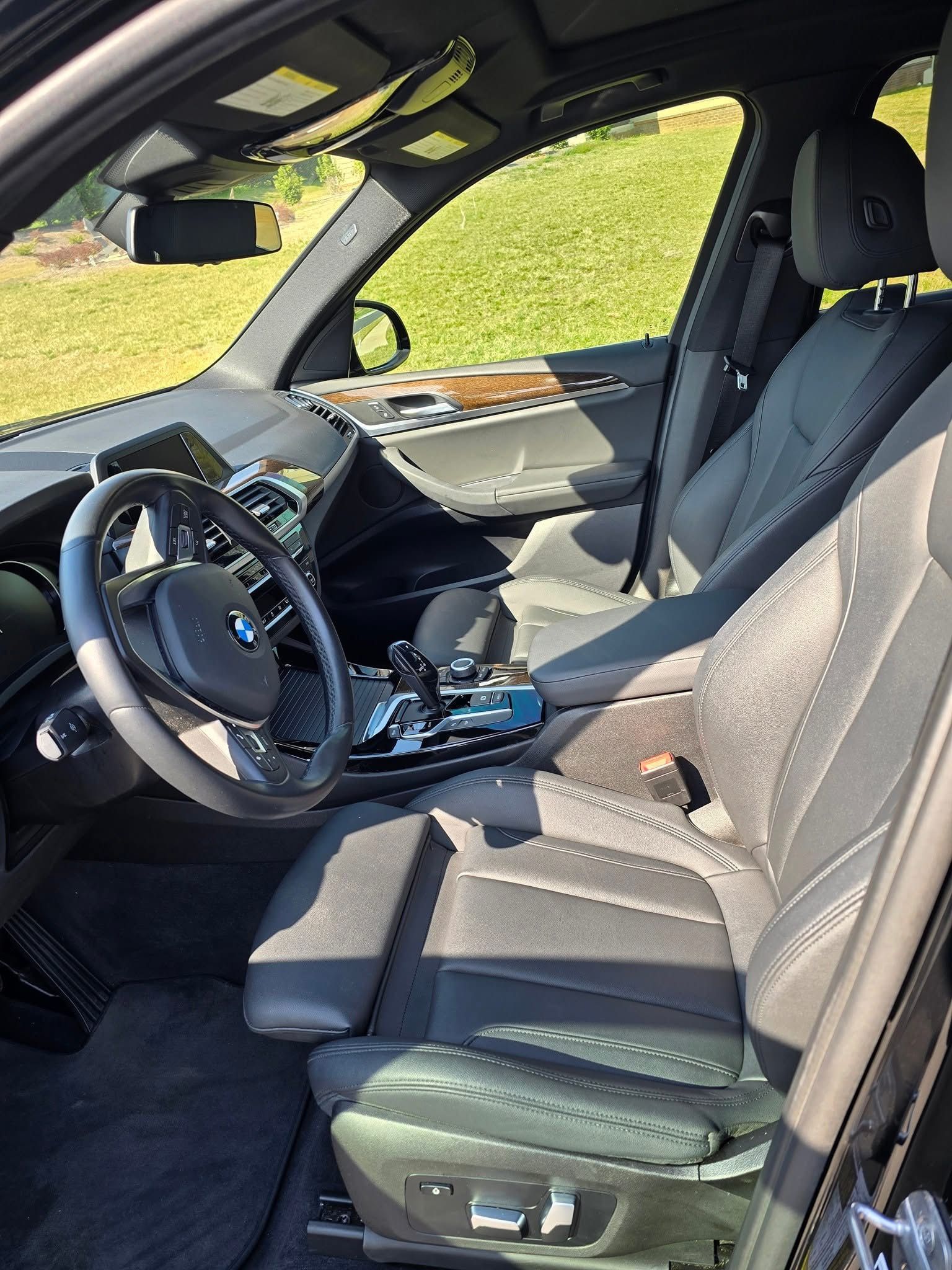 The interior of a black BMW SUV, showing the driver's seat, steering wheel, and dashboard on a sunny day.