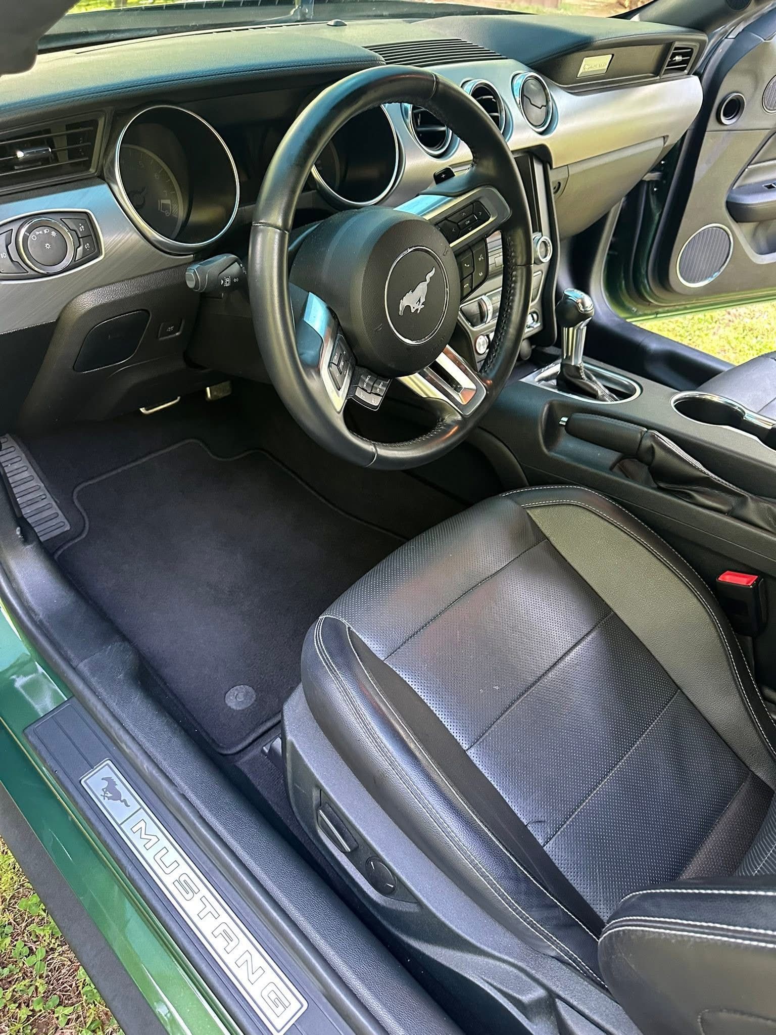 Interior view of a Ford Mustang featuring a dark leather driver’s seat, steering wheel, and dashboard.