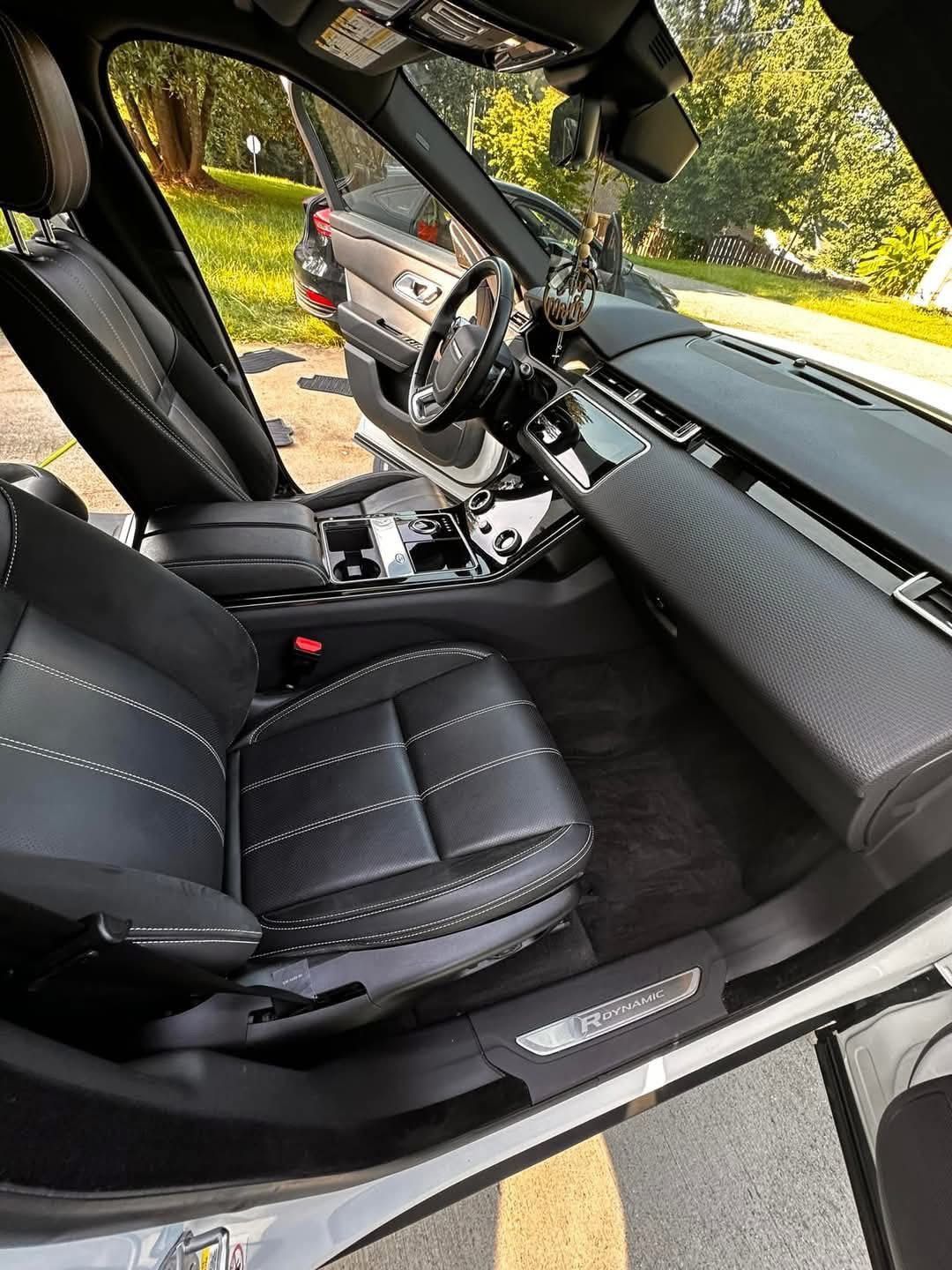 Interior view of a parked vehicle featuring black leather bucket seats, a dashboard with textured panels, and open doors.