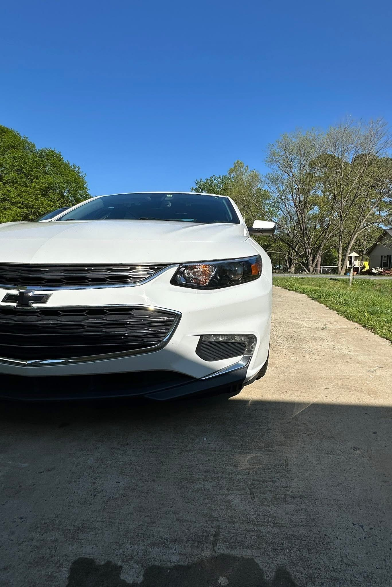 A low-angle view of a white Chevrolet Malibu parked on a gravel driveway under a bright blue sky.
