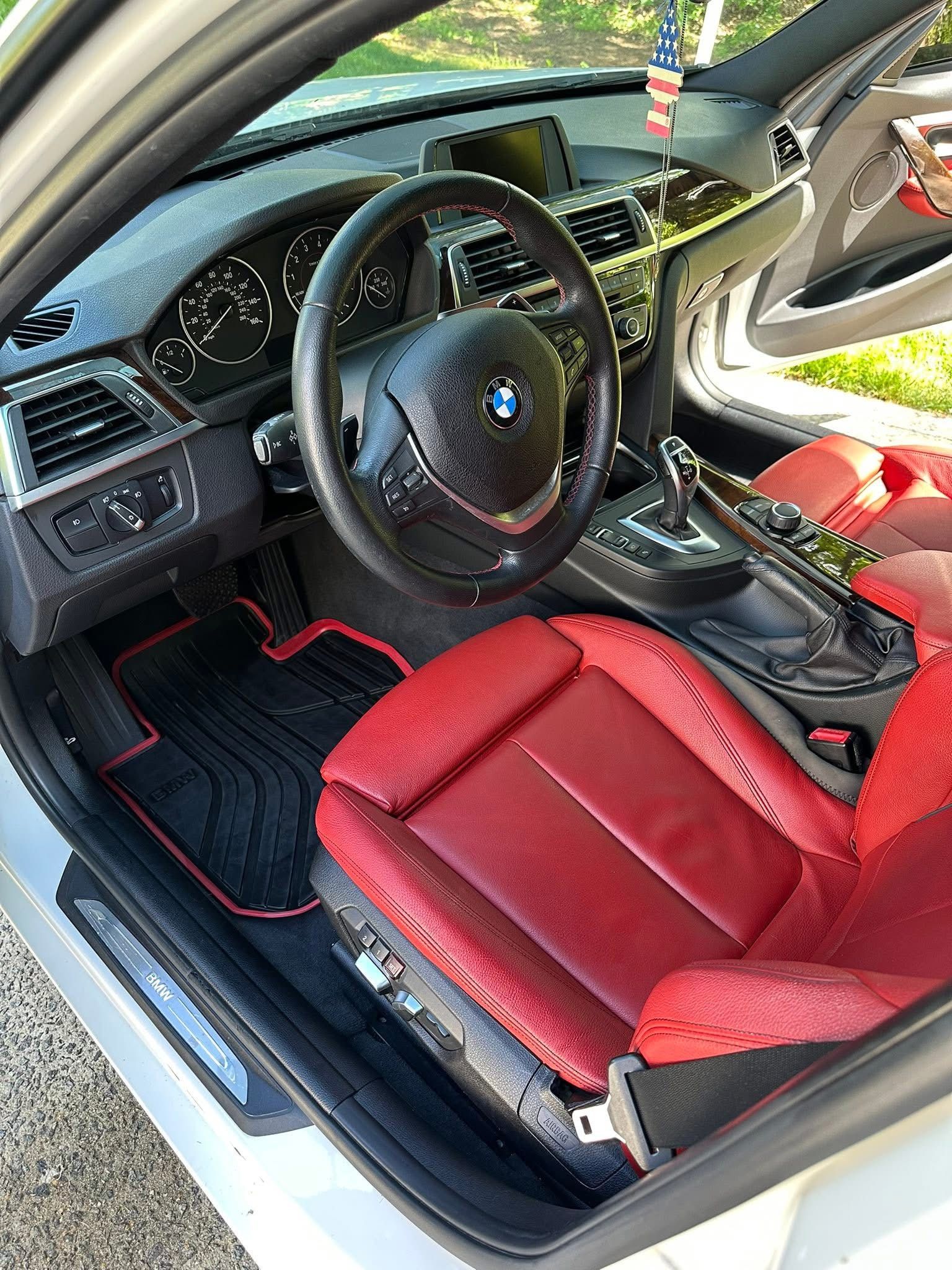 Interior of a BMW featuring a black dashboard, steering wheel, and floor mats with red trim, plus red leather seats.