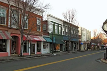 A street view of a small town row of historic brick buildings with storefronts and a clock on the sidewalk.