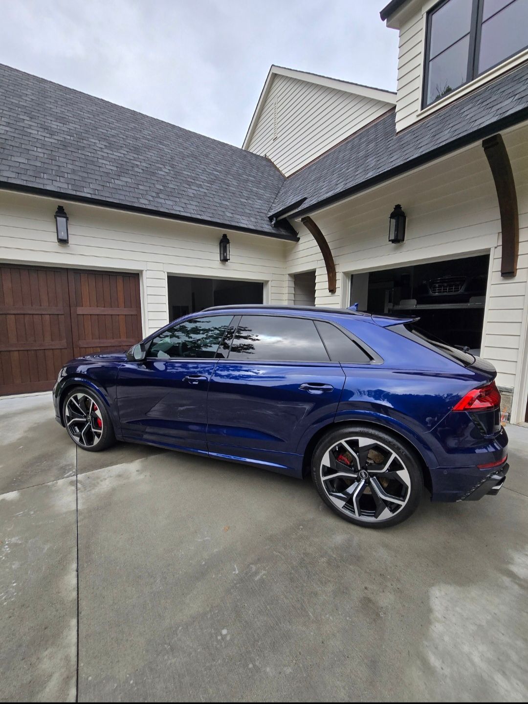 A dark blue Audi Q8 SUV parked in a concrete driveway in front of a multi-car garage of a suburban home.
