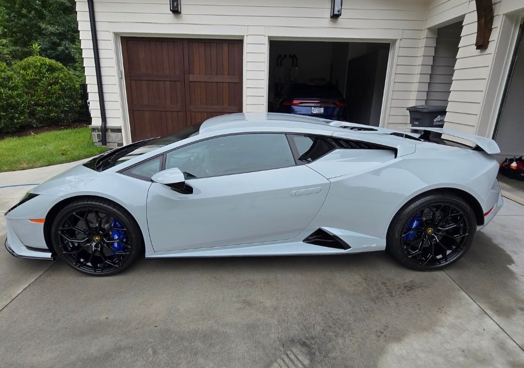 A light grey Lamborghini Huracán parked in a residential driveway in front of a garage.