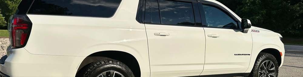 Side view of a white full-size SUV parked on a gravel surface with dark wheels and window visors.