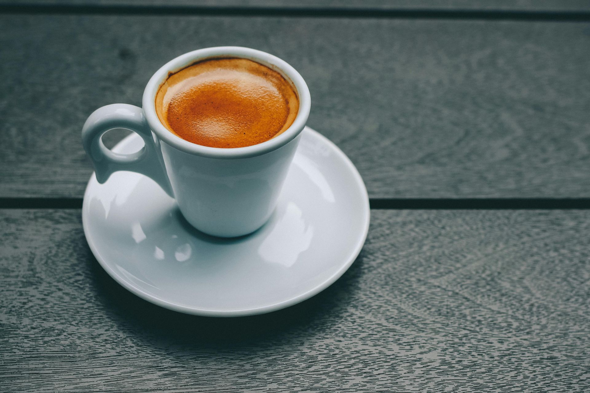 Espresso in a white cup and saucer on a gray wooden table.