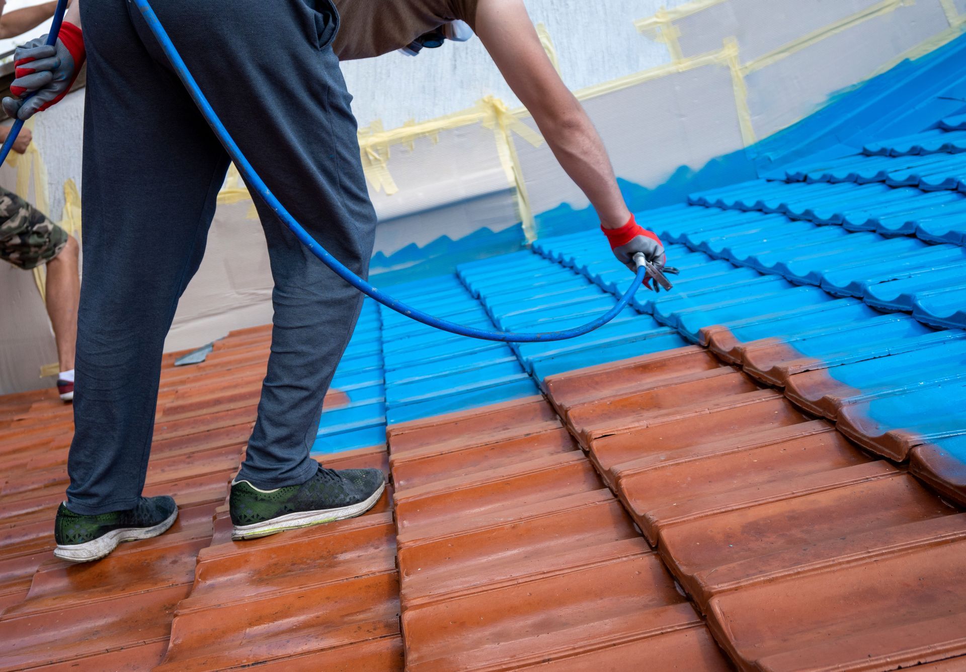 A cropped view of a roofer covering old roof tiles with a protective paint layer. A cropped view of a roofer covering old roof tiles with a protective paint layer.