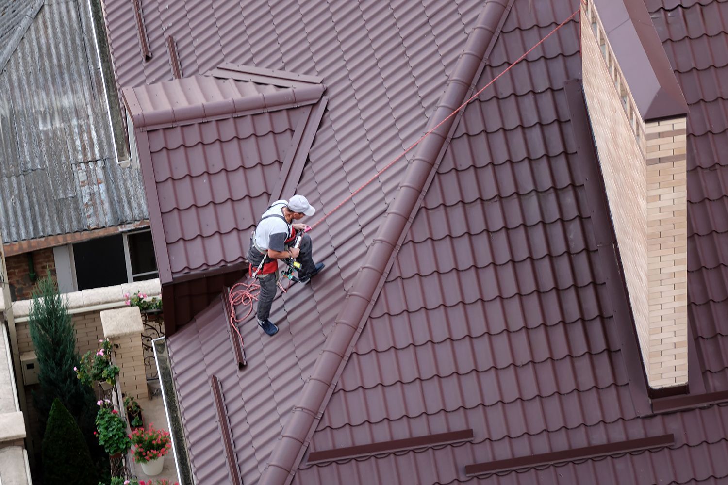 An aerial view of a roofer carrying out maintenance and roof restoration of metal profiles for a roof.