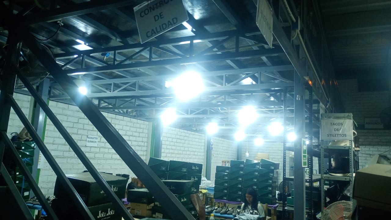 Almacén industrial oscuro con cajas negras apiladas, vigas de metal y luces brillantes en el techo.