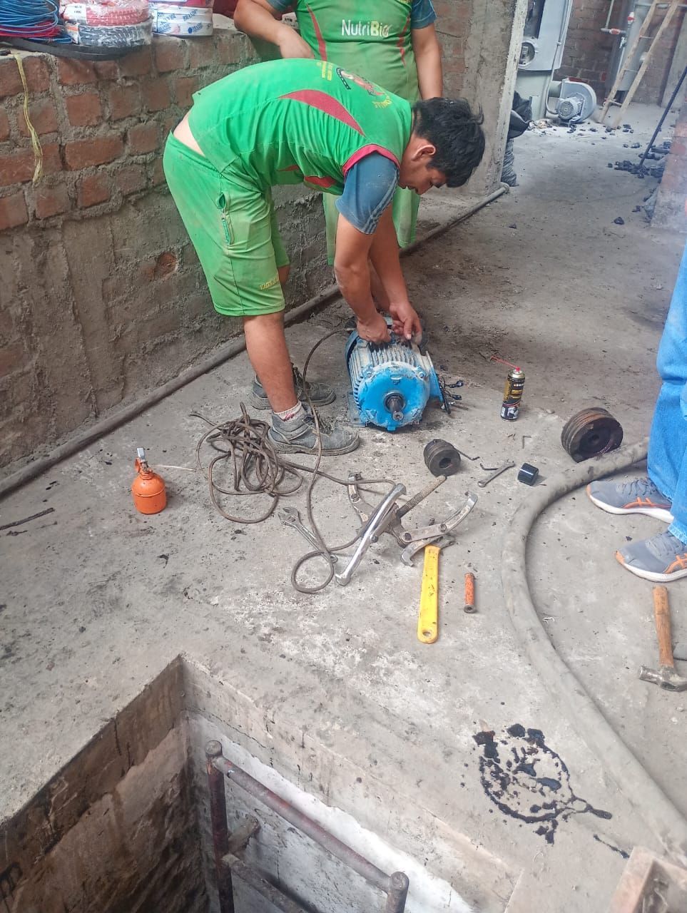 Un trabajador se inclina sobre una tubería azul en un suelo de hormigón, utilizando herramientas en una obra de construcción.