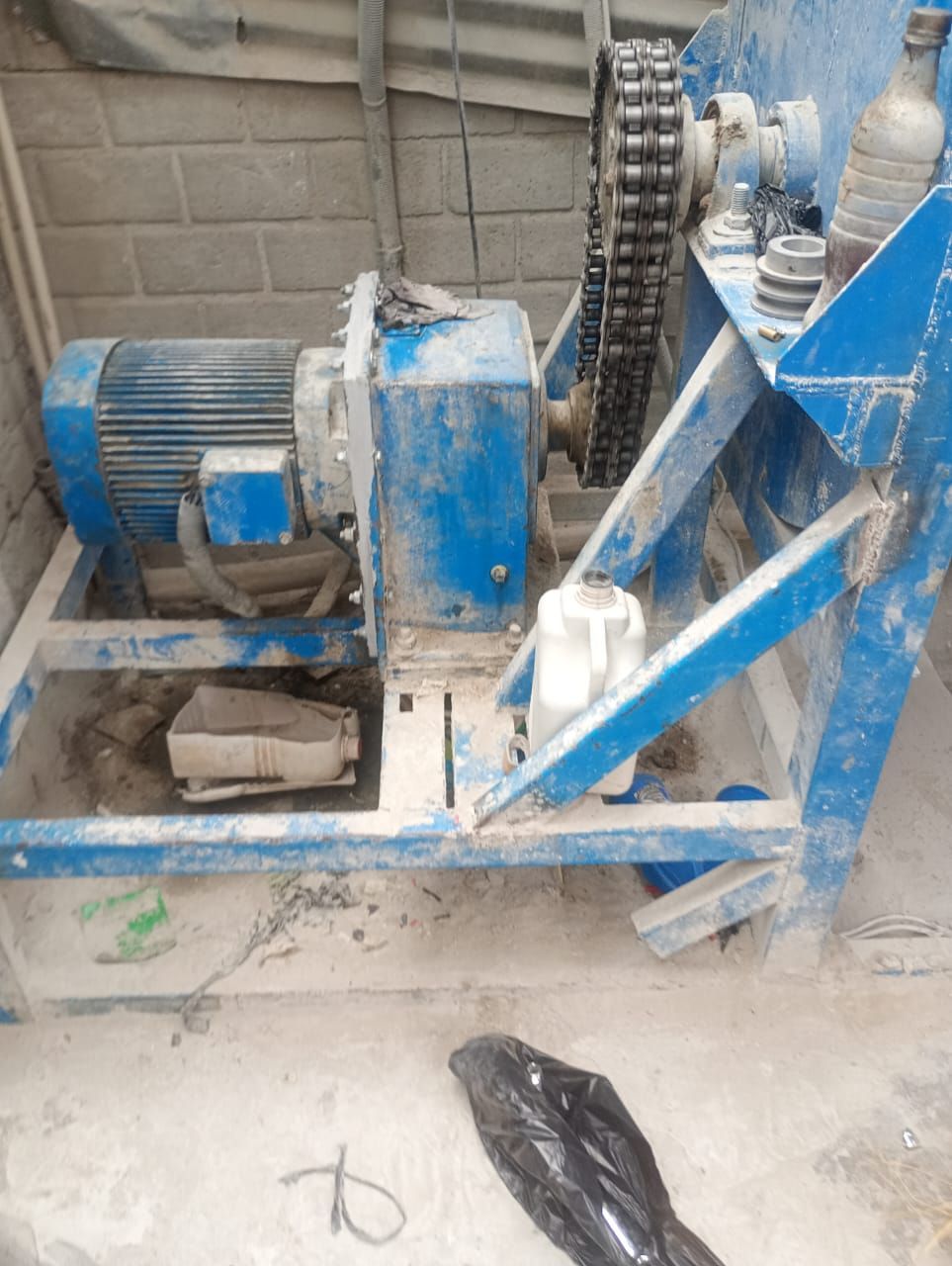Máquina industrial azul con motor y transmisión por cadena en un taller, sobre un suelo polvoriento.
