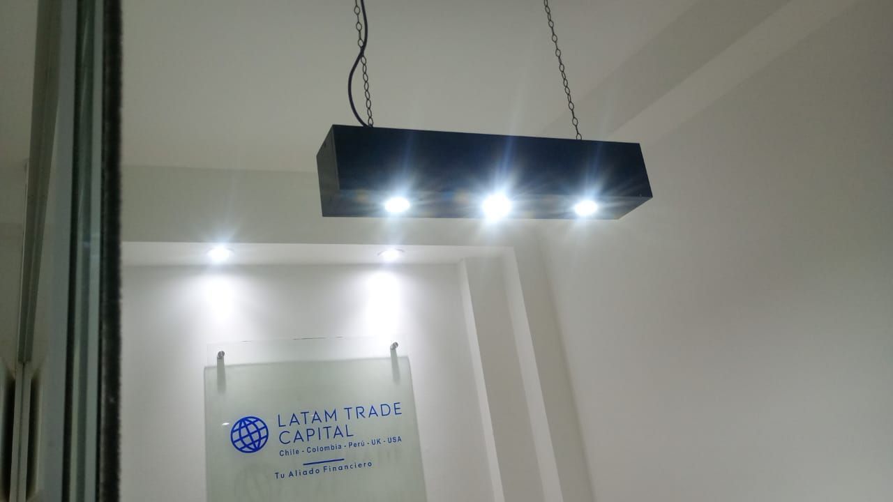 Lámpara de techo rectangular negra con LED brillantes que iluminan una habitación blanca y un letrero en la pared.