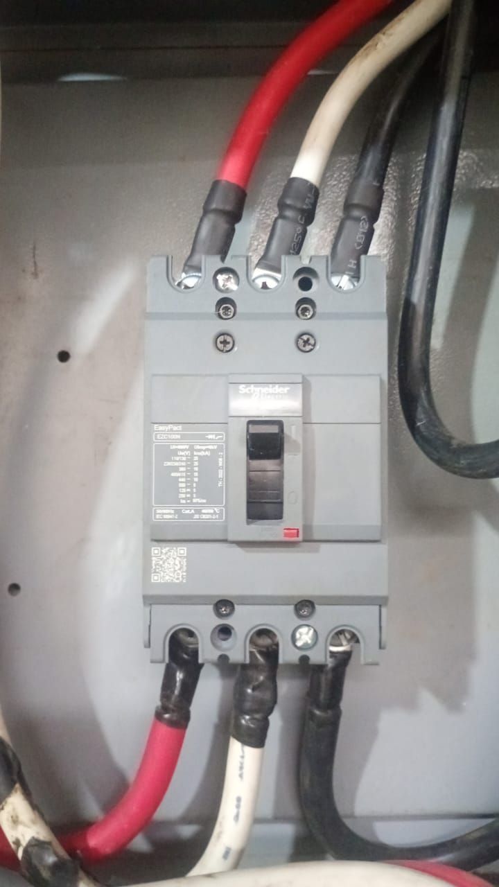Panel de disyuntores eléctricos con cables gruesos de color rojo, negro y blanco conectados al mismo.