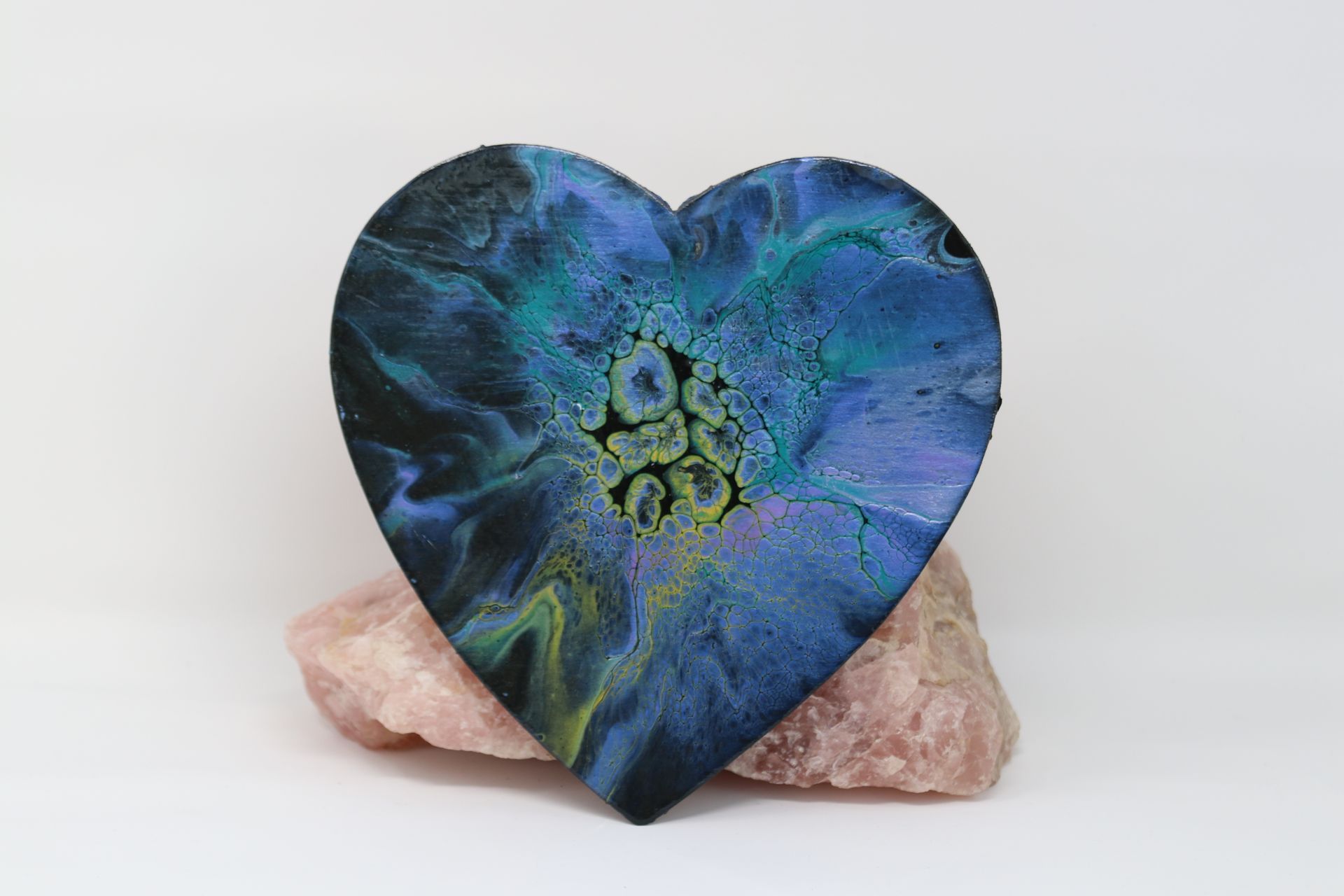 Blue heart-shaped crystal on a pink stone against a white background