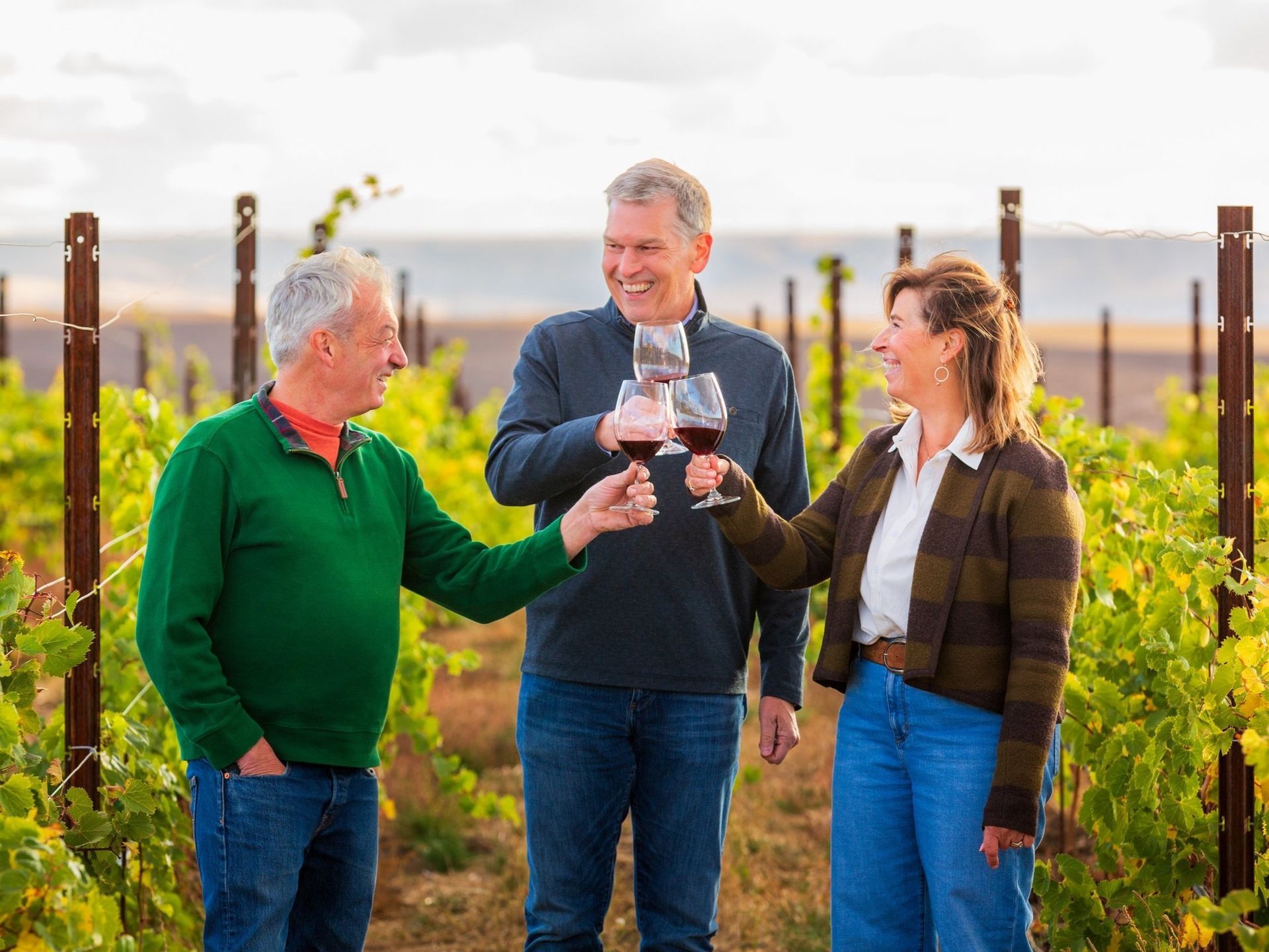 Ken, Kristin, and Serge cheers-ing their wine glasses in the vineyard