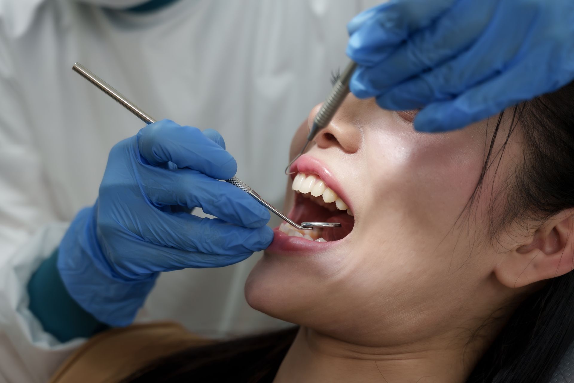A dentist wearing gloves and using dental tools during a patient procedure. A dentist wearing gloves and using dental tools during a patient procedure.