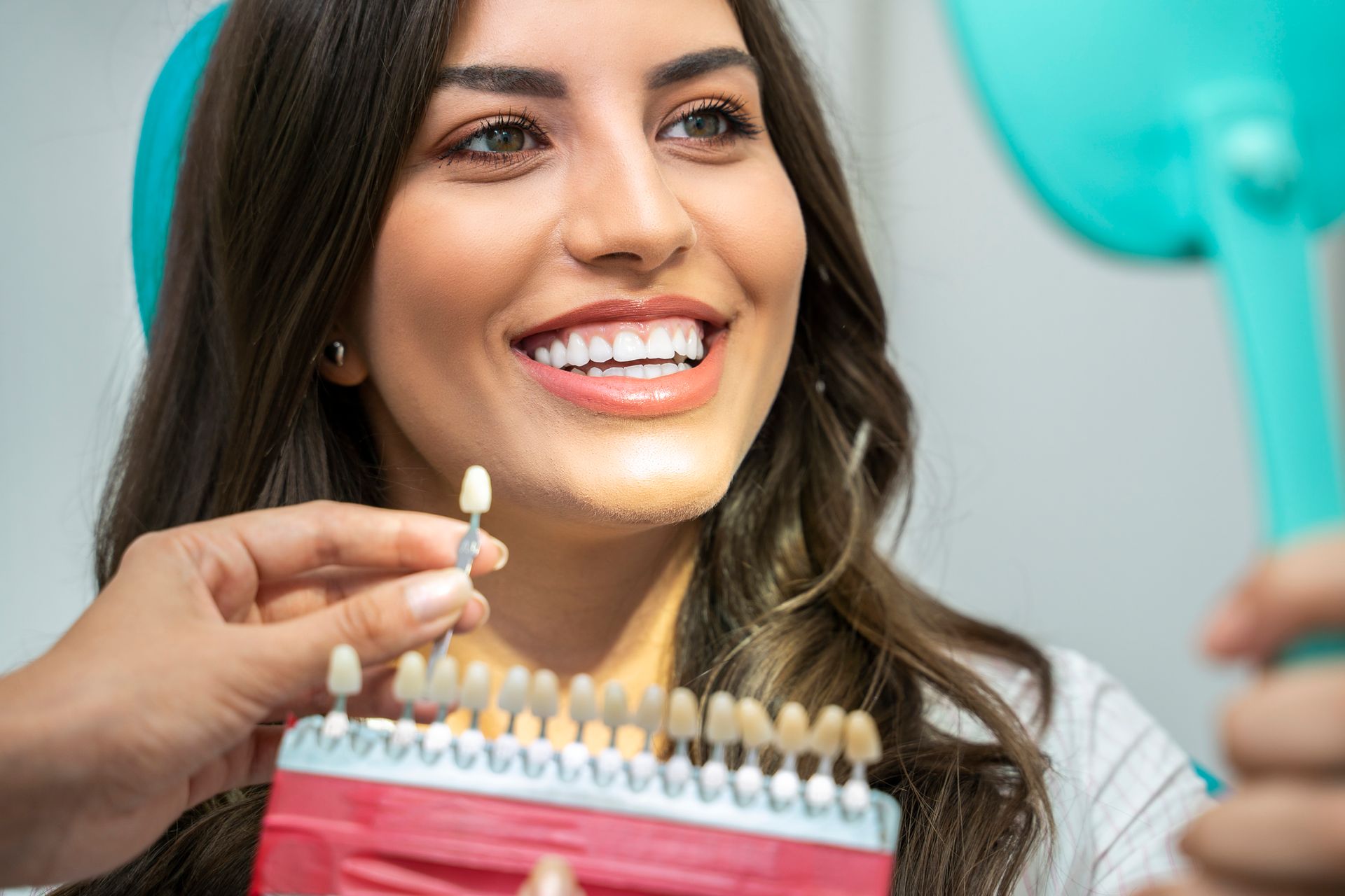 A woman is smiling while looking at her teeth in a mirror.