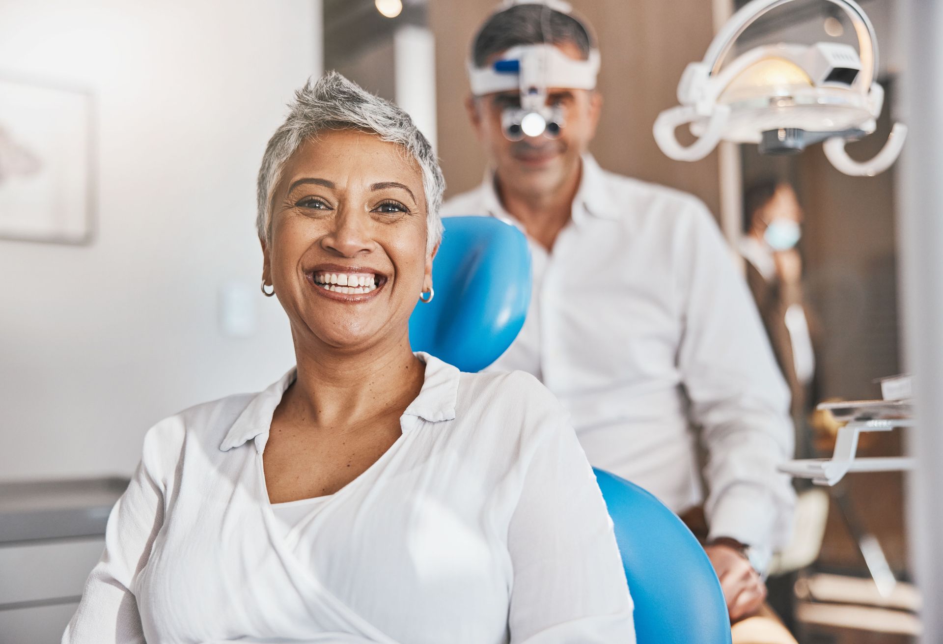 A woman is smiling while sitting in a dental chair.