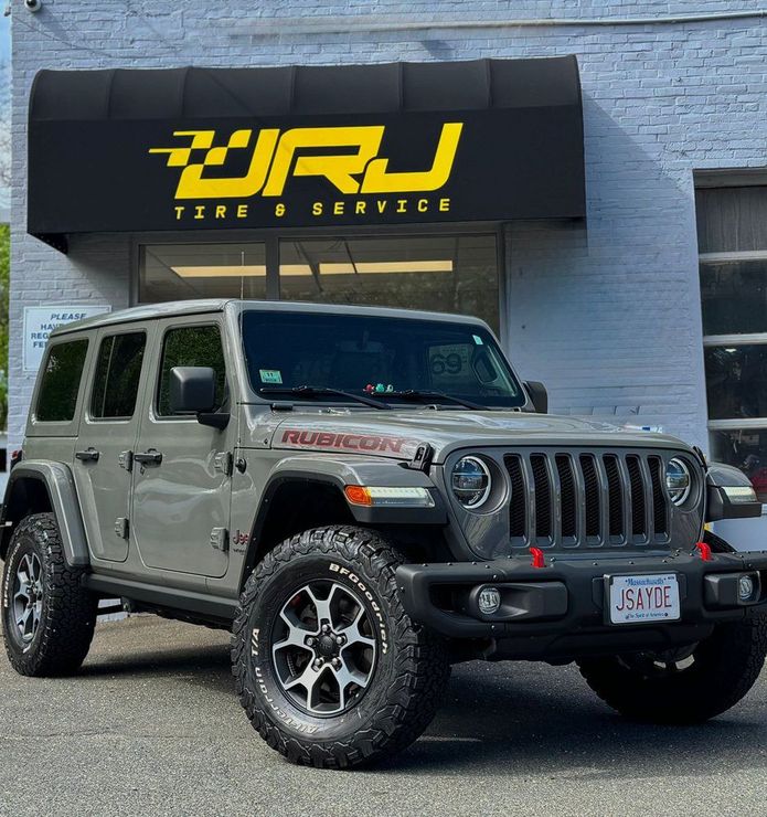 Gray Jeep Wrangler parked outside a tire shop with a yellow JRJ Tire & Service sign above | JRJ Tire & Service