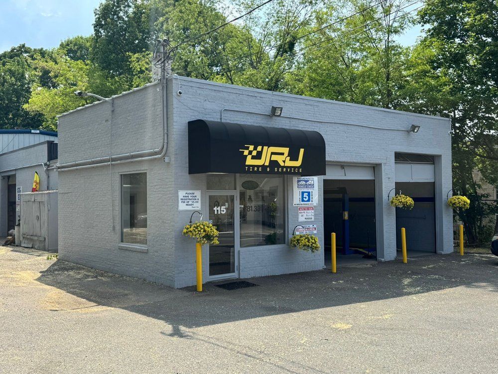 Small gray storefront with a black awning, yellow accents, and flower baskets in a parking lot | JRJ Tire & Service