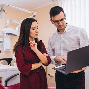 Two people reviewing a laptop in a dental office, with dental equipment in the background