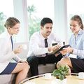 Three colleagues meeting on a sofa, reviewing a tablet with coffee cups on the table.