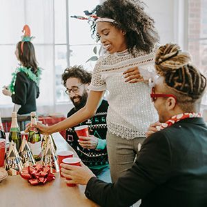 Friends chatting and reaching for drinks at a festive party table with decorations and red cups
