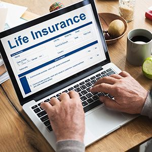 Hands typing on a laptop showing a life insurance webpage on a wooden desk with a coffee mug.