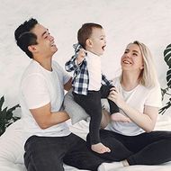 Smiling family sitting on the floor, playing with a toddler in a bright white room