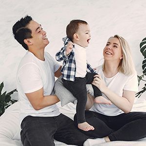 Smiling family sitting on the floor, playing with a toddler in a bright white room