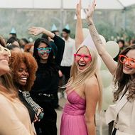 Friends dancing and smiling at an outdoor party, wearing colorful sunglasses