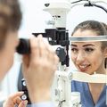 Eye exam in progress with a patient at a phoropter and an optometrist adjusting the machine