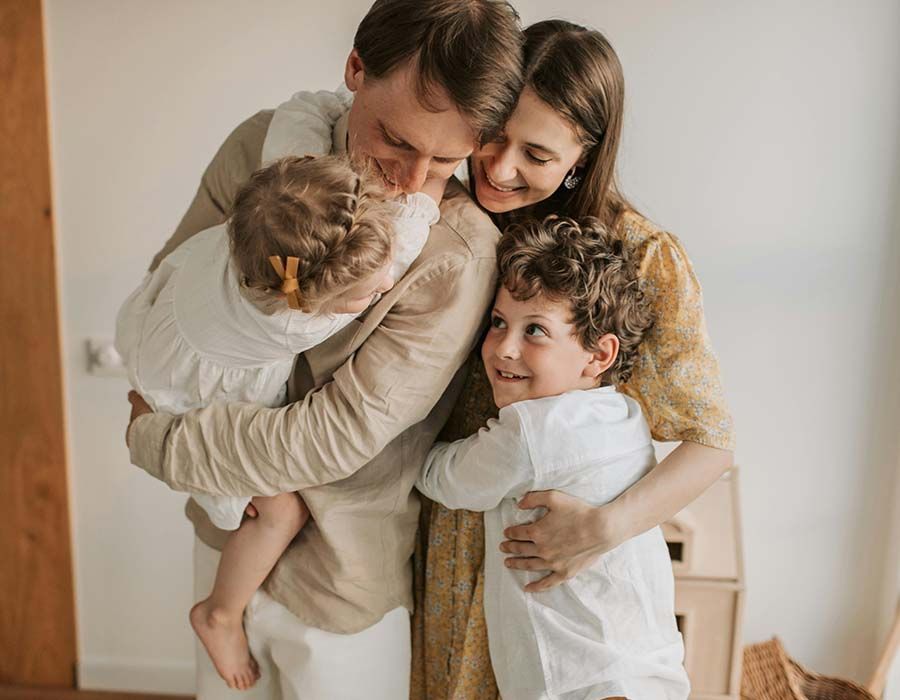 Family hugging together indoors, smiling warmly in a cozy, light-filled room