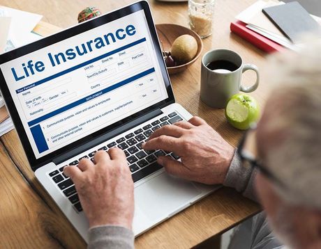 Hands typing on a laptop showing a life insurance website on a wooden desk with coffee mugs.